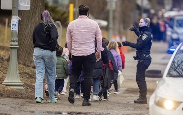 A police officer gestures to adults and children being led away from a school.