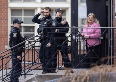 Three police officers stand on a staircase in front of a woman holding a door open.