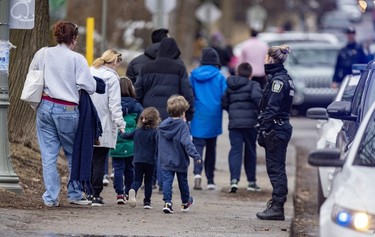 A police officer watches a group of adults and children walking down the sidewalk.