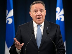 François Legault speaks at a podium in front of Quebec flags