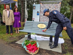 A man and woman watch their adult son place a rose on a commemorative bench honouring their daughter, in front of a poster for Mothers Against Drunk Driving.