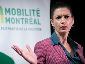 Genevieve Guilbault is seen gesturing with her hand up in this photo, while wearing a pink blazer over a blue shirt, standing in front of a sign that says 'mobilite montreal.'