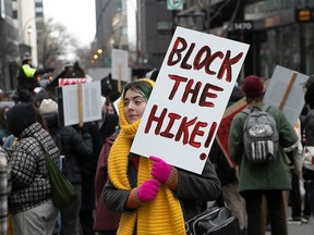 A person holds a sign reading 'block the hike!' during a protest on a street