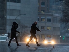 Two people cross a street in heavy winds and rain.