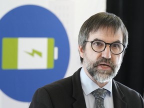 A close-up of bearded Environment Minister Steven Guilbeault is seen giving a talk in front of a pictogram of a battery.