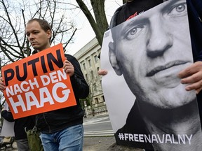 A demonstrator holds a portrait of Russian opposition leader Alexei Navalny and another one holds a placard reading "Putin to The Hague," on Feb. 16, 2024 in front of the Russian embassy in Berlin, after the announcement that the Kremlin's most prominent critic had died in an Arctic prison.