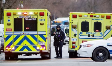 A police officer in heavy gear stands between two ambulances on a city street.