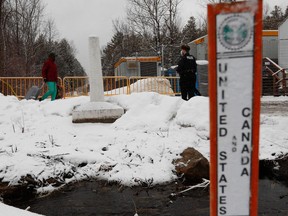 A police officer greets an asylum seeker behind a snowbank at Roxham Road, with a United States and Canada sign in the foreground.