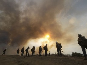 Firefighters watch as the Fairview Fire burns on a hillside, Sept. 8, 2022, near Hemet, Calif.