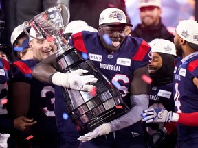 Lwal Uguak smiles while holding the Grey Cup on a stage with teammates as confetti falls from the sky