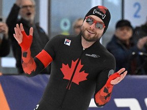 Laurent Dubreuil raises his hands and smiles while wearing a speedskating suit