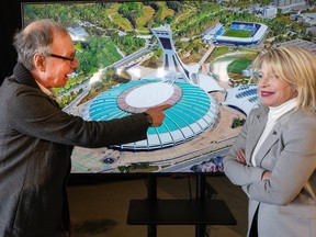 Michel Labrecque, president and director general of the Olympic Park installations, and Quebec Tourism Minister Caroline Proulx stand in front of an illustration of Montreal's Olympic Stadium. They're facing each other and Labrecque is pointing at the stadium.