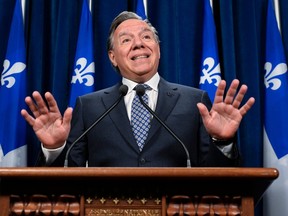 François Legault gestures while speaking at a podium with Quebec flags behind him