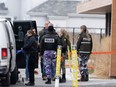 Police officers congregate near a police vehicle and crime-scene tape.