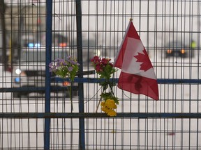 A small Canadian flag and flowers are shown on temporary fencing in downtown Ottawa on Sunday, Feb. 20, 2022.