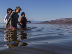 Francesca Gambini, left, Cara Tan, centre, and Alejandra Pulido laugh as the return to shore after trying to cross on a temporary lake on foot in Death Valley on Thursday, Feb. 23, 2024, in Death Valley National Park, Calif.