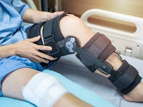 The legs of a person in a hospital bed. One knee is in a compression device.