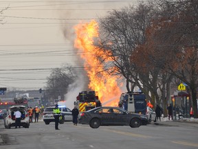 A fire truck is next to a tall blaze on a city street.