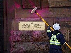 A worker removes pink paint from the exterior of the entrance to the prime minister's office on Wellington St. in Ottawa on Wednesday, Feb.7, 2024.