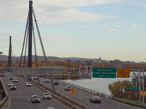 A photo of a bridge is seen in the left of frame with cars crossing over. There is a river on the right of the frame and land can be seen on the other side.