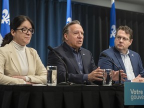 Quebec Premier François Legault is flanked by Treasury Board President Sonia LeBel and Education Minister Bernard Drainville at a table during a news conference.