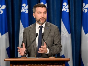 Québec solidaire co-spokesperson Gabriel Nadeau-Dubois speaks at a podium while gesturing with his hands, with Quebec flags in the background.