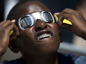 A boy with braces looks up at the sun with eclipse glasses.