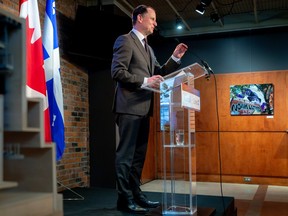 A man speaks at a press conference. He's standing at a clear podium and there are Canadian and Quebec flags behind him.