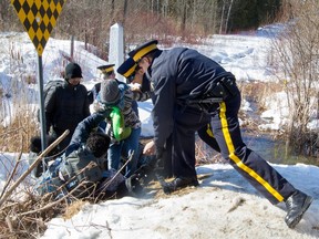 RCMP officers help a group of asylum seekers to cross a ditch as they crossed from the U.S. into Canada illegally at the border at Roxham Road in Hemmingford, south of Montreal, on Feb, 20, 2017.