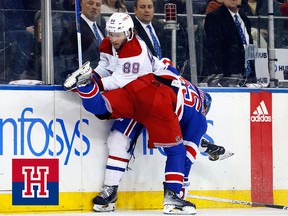 A hockey player is checked into the boards by an opponent whose upper body is parrallel to the ice