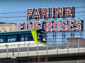 A commuter train passes a large neon sign that says Farine Five Roses