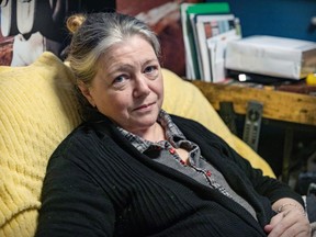 A woman with grey hair is sitting in a large chair with a yellow blanket over it. She is wearing black.