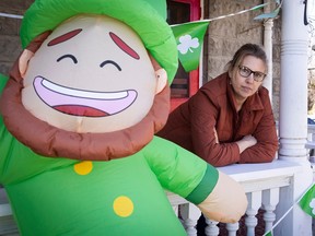 A woman leans on a porch rail, looking serious. In the foreground is a blowup St. Patrick's leprechaun.