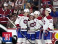 Four hockey players celebrate a goal together in front of cheering fans