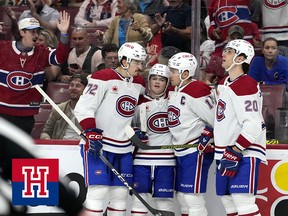 Four hockey players celebrate a goal together in front of cheering fans