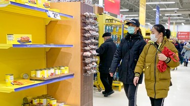 Two people walk past empty shelves in a grocery store.