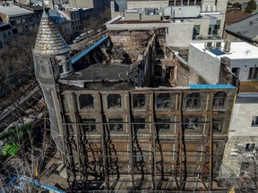A hollowed out building is seen from above, nearly a year after a fire swept through it. The exterior stone walls are being held up by wooden beams.