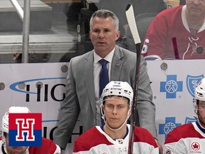 Martin St. Louis, wearing a suit, stands behind Montreal Canadiens players seated on the team's bench