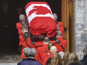 Pallbears are seen from behind carrying a casket covered with a Canadian flag.
