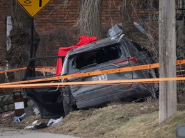 A car is crashed into a tree and is surrounded by crime-scene tape.