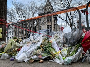 A pile of flowers is seen on the ground in the foreground of this picture, beneath a banister and danger tape and, in the background, a hollowed out building.