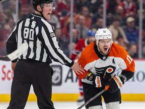 Philadelphia Flyers' Travis Konecny grimaces while hunched over as a linesman yells over his shoulder