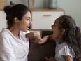 A mother and her young daughter speak to each other on a couch,.