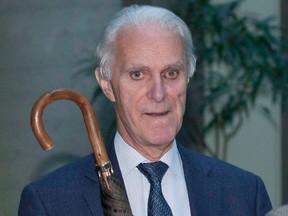 Jacques Delisle wears a suit and holds a closed umbrella while indoors