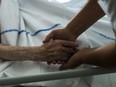 Closeup shows hand of nurse holding hand of palliative care patient in a medical setting.