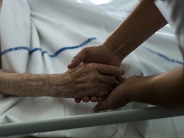 Closeup shows hand of nurse holding hand of palliative care patient in a medical setting.