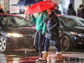 Montrealers shelter themselves from the rain as they cross Ste-Catherine St. at Peel in pouring rain in Montreal on Dec. 26, 2016.