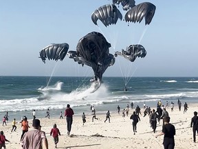 This image grab from an AFPTV video shows Palestinians running toward parachutes attached to food parcels, air-dropped from U.S. aircraft on a beach in the Gaza Strip on Saturday, March 2, 2024. Israel's top ally the United States said it began air-dropping aid into war-ravaged Gaza on March 2, as the Hamas-ruled territory's health ministry reported more than a dozen child malnutrition deaths.