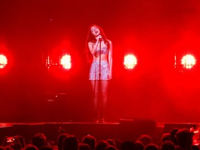 A woman in silver sings into a microphone with red lights surrounding her.