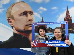 Women pose in front of a mural depicting Russian President Vladimir Putin after voting in Russia's presidential election.